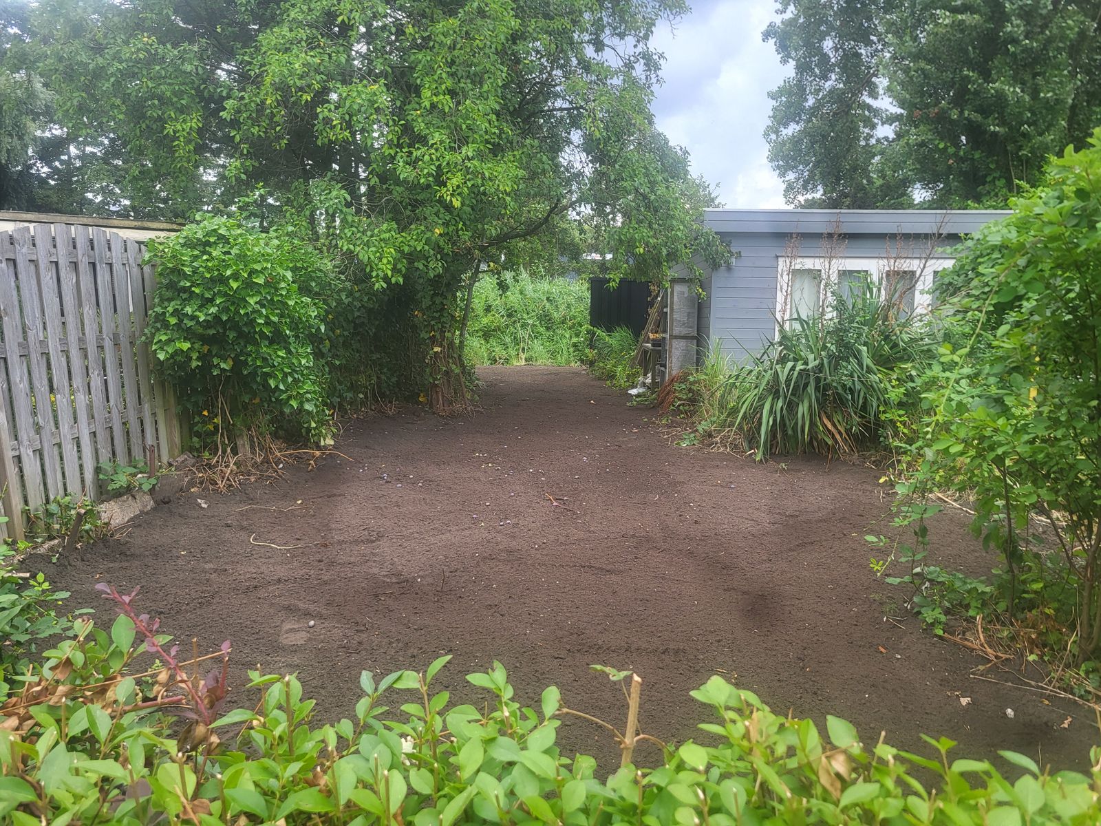 Leeggemaakte achtertuin met zwarte aarde naast tuinhuis